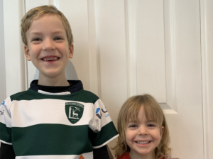 Two boys, Jacob and Harrison Dearing, in a green and white top and a red top smile with a rugby ball