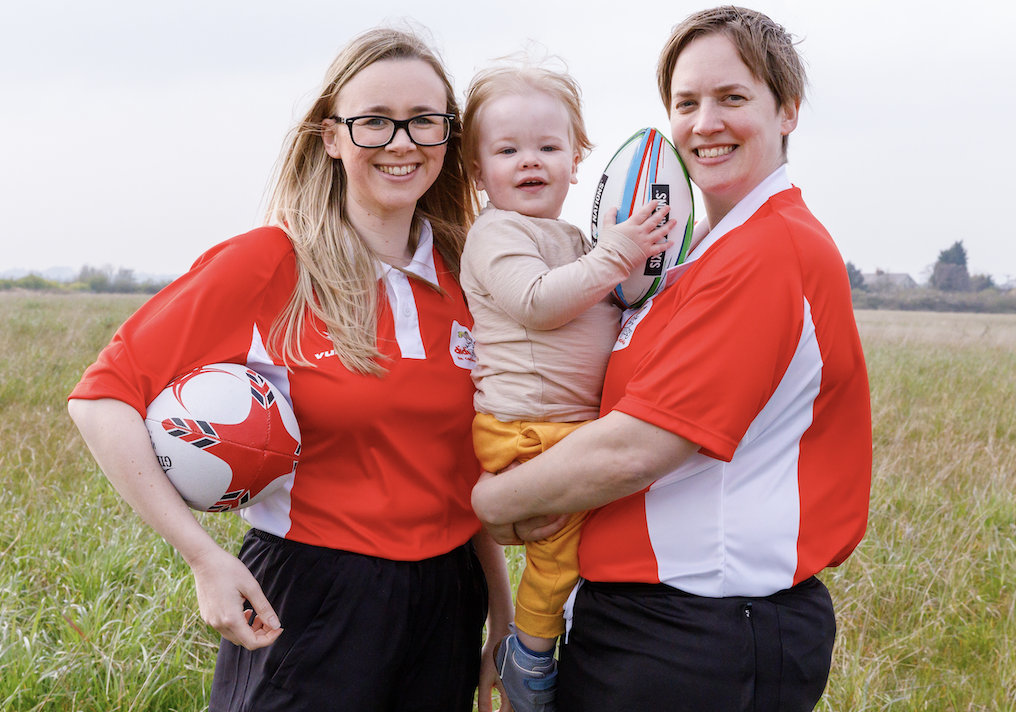 Sophie and Hattie Elliott-Edwards stand together with young son Oliver wearing red didi rugby tops