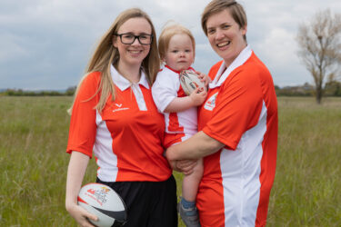Sophie and Hattie Elliott-Edwards wearing red didi rugby kit, holding their son, Oliver.