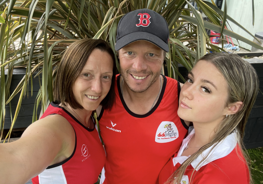 Two ladies in a red top and a man wearing a red top and blue cap smile