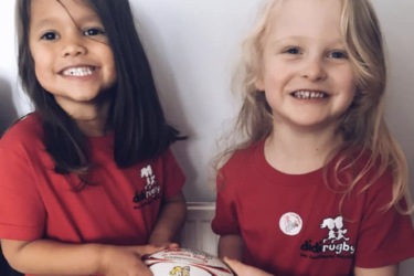 Two girls wearing a red didi rugby T-shirts holding a didi rugby ball