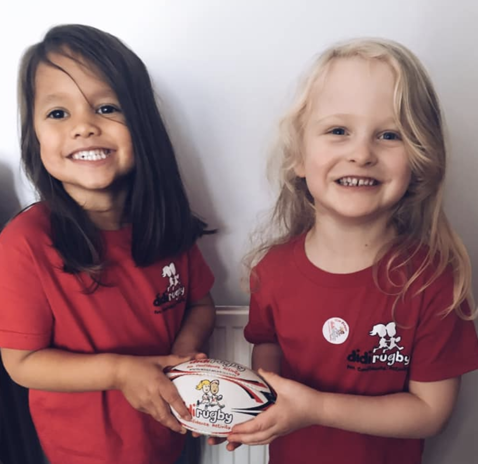 Two girls wearing a red didi rugby T-shirts holding a didi rugby ball