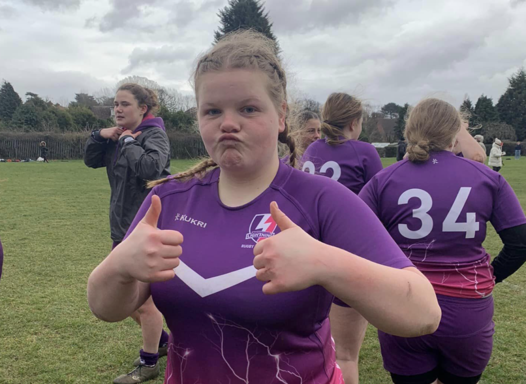 A girl in a purple rugby top gives both thumbs up to the camera