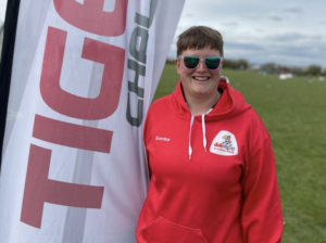 didi rugby Sandbach coach Ros Wiggins smiles wearing a red didi rugby hoodie and sunglasses